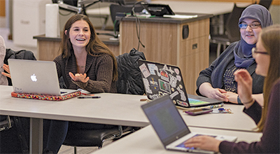 Students talk to each other across a table with their laptops