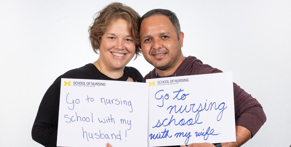 Eddie and Tamara Villavicencio hold signs that say &quot;go to nursing school with my wife&quot;