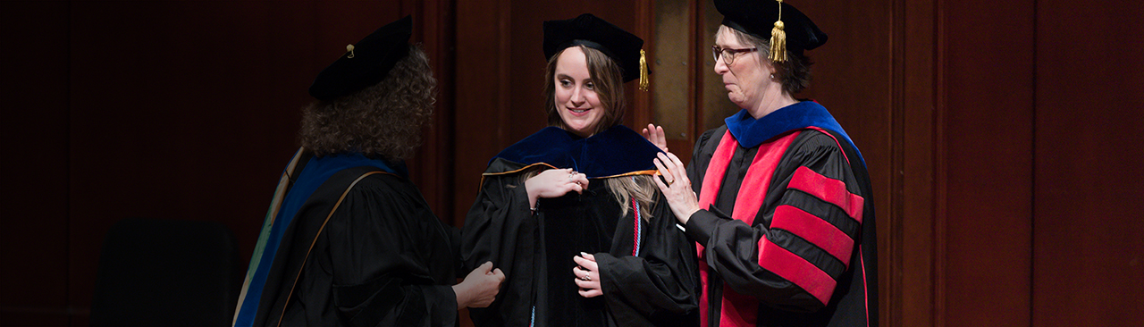 Student gets hooded at graduation by faculty member in robes. 