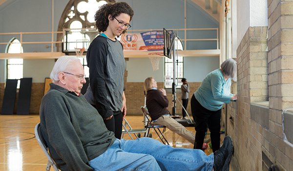 Woman looking at a older man sitting in a chair in a gym while doing research.