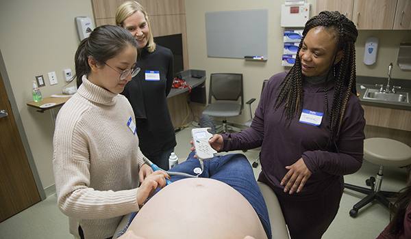 Three midwifery students examine pregnant patient 