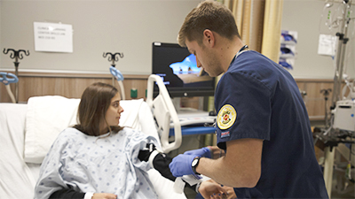 Undergraduate University of Michigan student practicing on a patient who is in bed