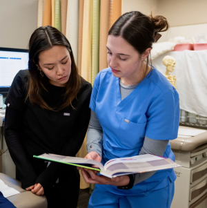 Two female nursing students attentively studying a book together, deep in thought and focused on their task.