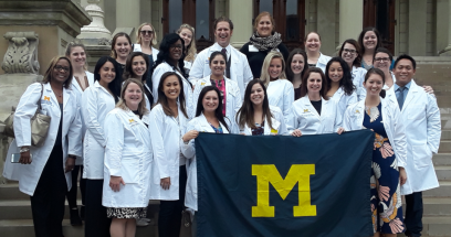 Group of students in white coats holding a block M flag